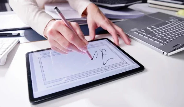 image d'une personne utilisant un stylet pour signer ou annoter un document sur une tablette numérique, dans le cadre de la gestion de contrats de maintenance.